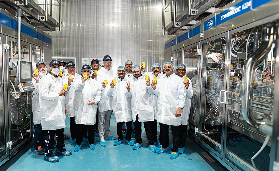 The image features a group of people, Amul Dairy team employees, in a factory,posing for a picture,wearing lab coats. There are at least 11 people visible in the image.