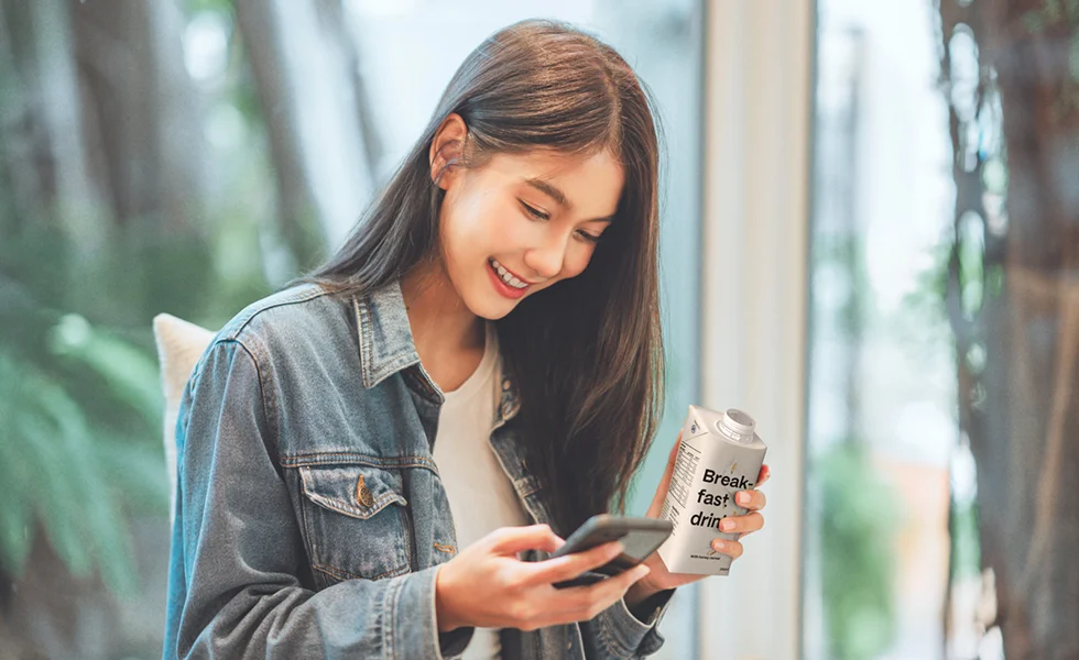 A woman holding a drink packaged in the SIG packaging, looking at her phone (photo)