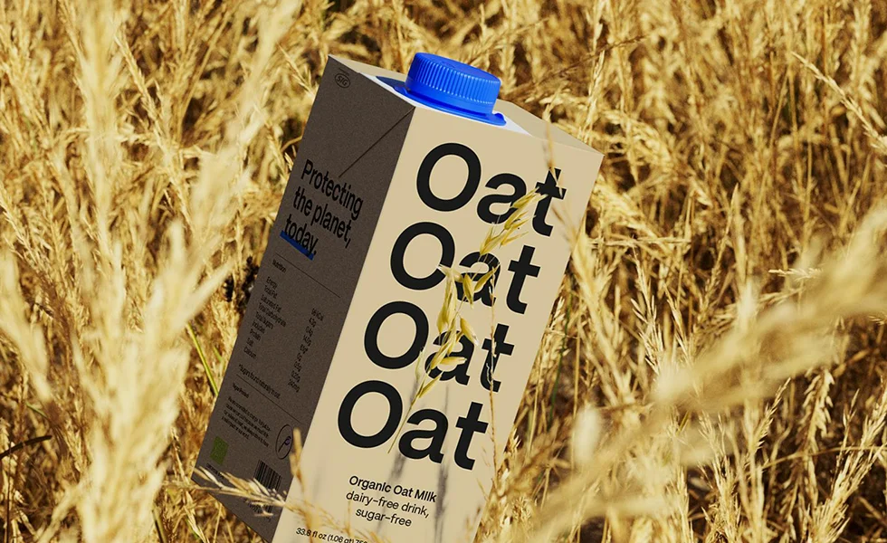 The image features a carton of Oat drink in a field of wheat.