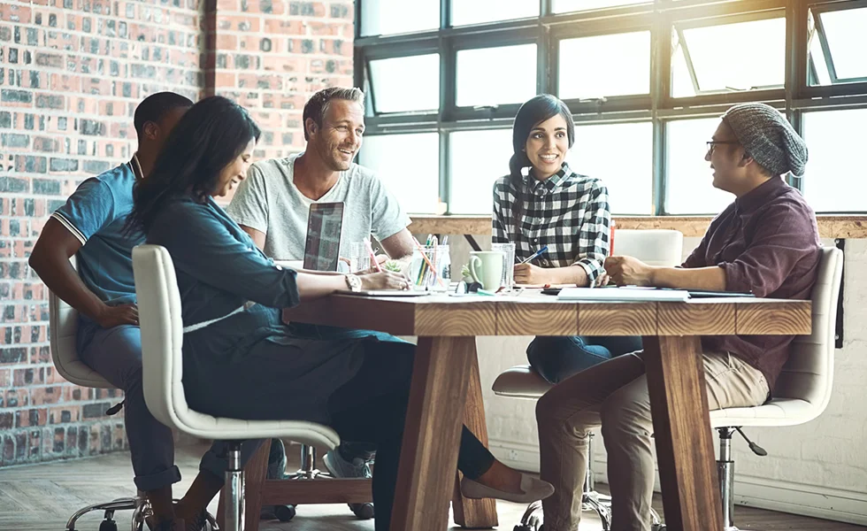 The image features a group of people sitting around a large dining table, engaged in conversation and enjoying each other's company.