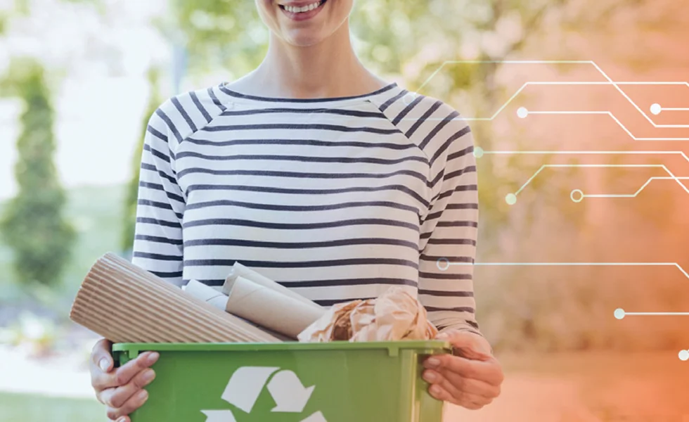 In the image, a woman is standing and holding a recycling bin or waste paper basket. She is wearing a striped shirt, and the background features a tree. The scene appears to be set in an outdoor location, possibly a park or a street.