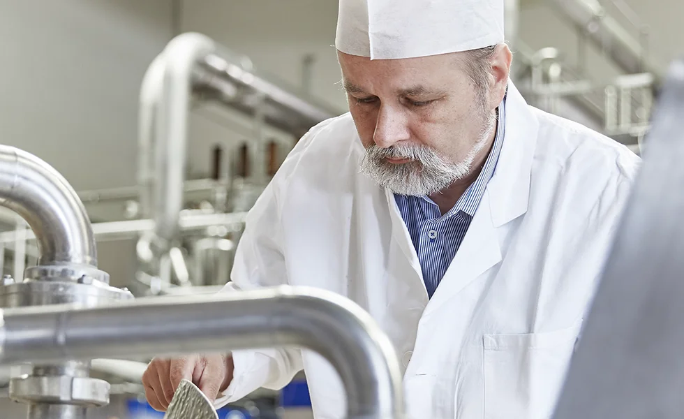 The image features a man in a white lab coat working in a factory or lab setting.