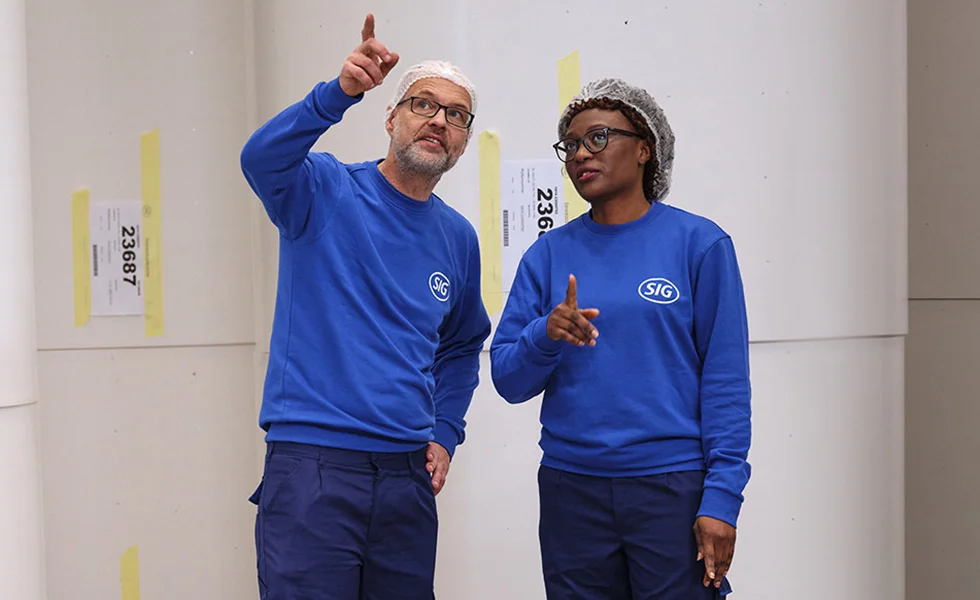 The image features a man and a woman standing next to each other, both wearing blue shirts. They appear to be pointing in the same direction, possibly engaged in a conversation or indicating something in the distance.