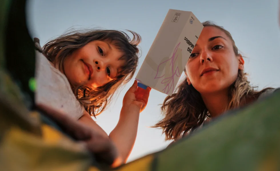 The image features a woman and a young girl, who appear to be a mother and her daughter. They are holding up a piece of paper, possibly a card or a note, as if they are reading or discussing it.