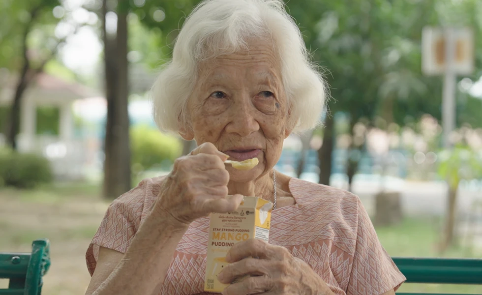An elderly woman eating mango pudding while sitting outdoors (photo)