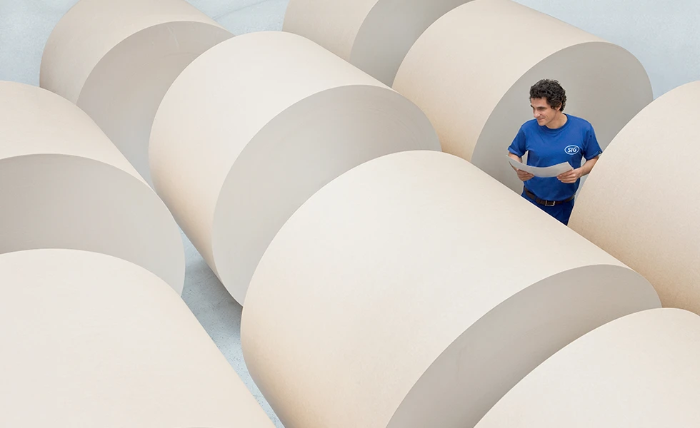 A man holding papers while standing among large rolled paper reels (photo)