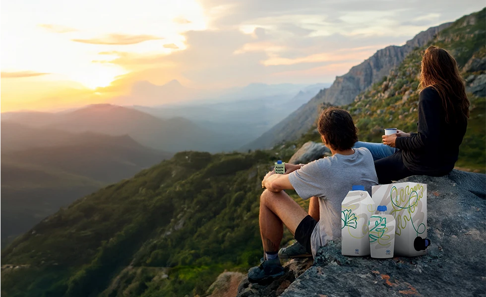 Two people sitting on a mountain cliff with drinks, overlooking a scenic valley. (photo)