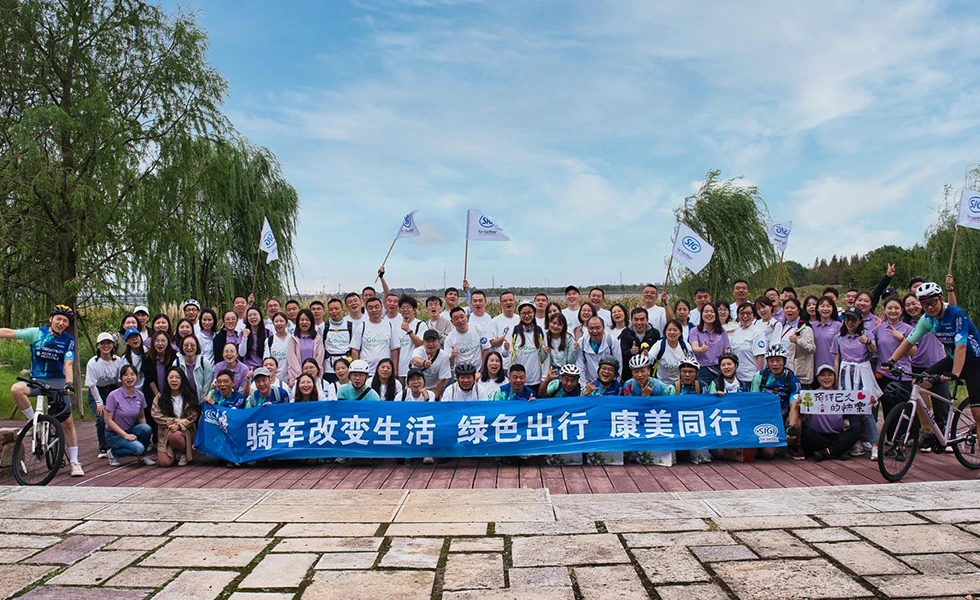 A large group of SIG employees in China posing outdoors with a banner and bicycles. (photo)